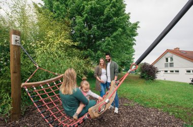 Spielende Familie auf dem Spielplatz Blofeld, Mutter schaukelt mit Kind