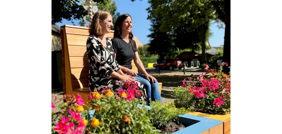 Bürgermeisterin Lena Herget und Sandra Sibbe von der „Alten Blechwerkstatt“ genießen die neuen Stadtmöbel in Weckesheim